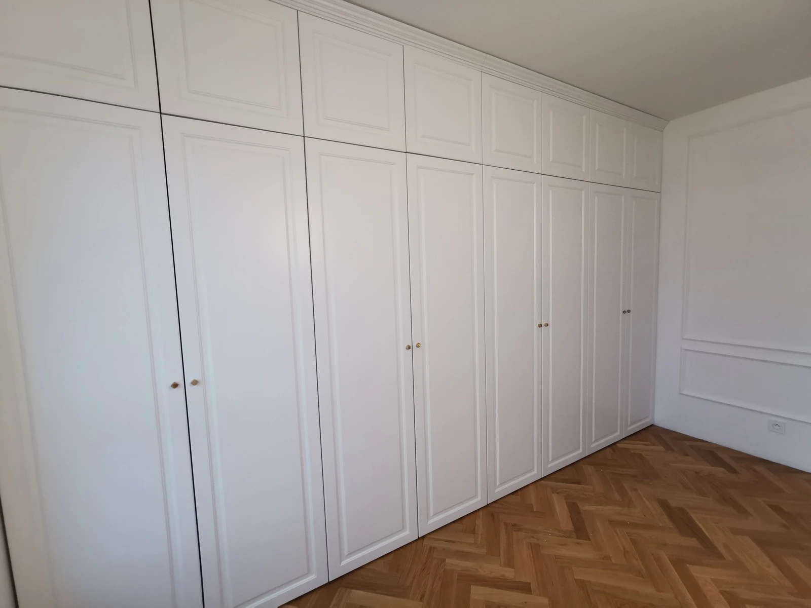 Biała szafa na wymiar z frezowanymi frontami i złotymi gałkami, narożna zabudowa pod sufit, Meble Mibu Gdańsk